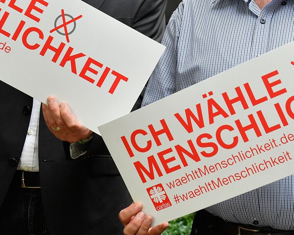 Zwei Personen halten Schilder mit der Aufschrift Wählt Menschlichkeit | © Caritasverband München und Freising e.V. 