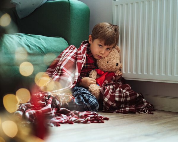 Ein Junge sitzt mit einer Decke vor einer Heizung am Boden | © istock | Yulia Raneva