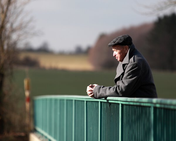 Ein älterer Mann steht an dem Geländer einer Brücke und schaut in die Ferne | © Tobias Schenk - ginkgofoto - Fotolia